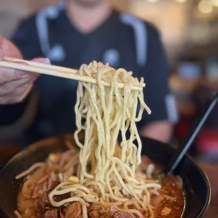 a person holding chopsticks over a bowl of ramen