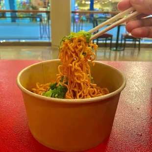 a person holding chopsticks over a bowl of noodles