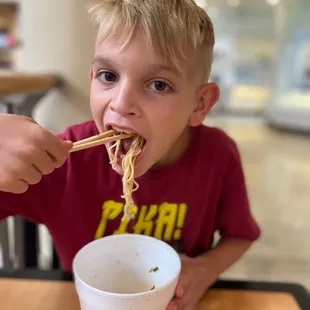 a young boy eating noodles with chopsticks