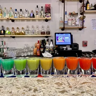 a variety of colored cocktails on a bar