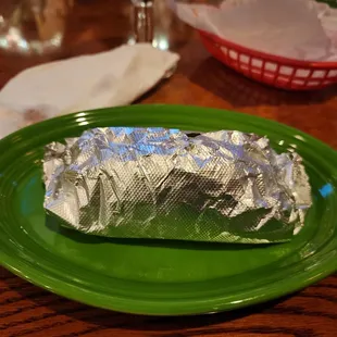 a burrito wrapped in aluminum foil on a green plate