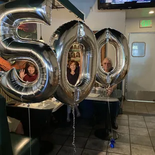 a group of people sitting at a table with large balloons in the shape of the number 50