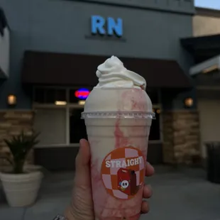 a hand holding a cup of strawberries and whipped cream