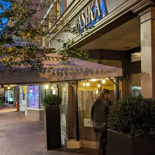 a woman walking down a sidewalk at night