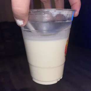 a hand holding a plastic cup of milk