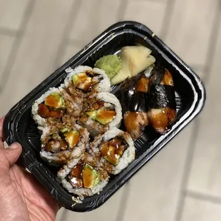 a hand holding a container of sushi