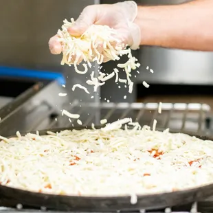 a person sprinkling cheese on a pizza