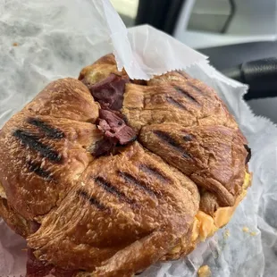 a hand holding a croissant sandwich