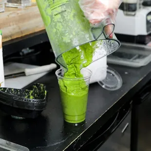 a person pouring green smoothie into a blender