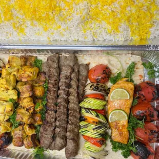 A party platter featuring fresh vegetables, grilled chicken and beef kabobs, and salmon.
