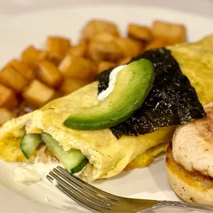 an omelet with avocado on top and a side of potatoes