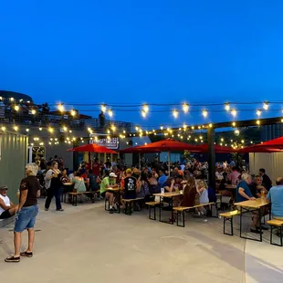 a crowd of people sitting at tables under red umbrellas