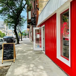 a red building with a sign on the sidewalk