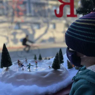 The littlest human enjoys the winter scene set up at Red Rocks, outside, a bicyclist passes. This is a quintessential Mountain View scene.