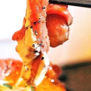a piece of meat being held by a pair of chopsticks