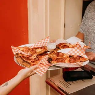 a person handing a plate of pizza