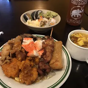 A mix of several chicken dishes. Pot stickers, pork egg roll, some sushi, some egg drop soup.