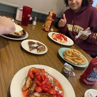 a girl sitting at a table with french toast and strawberries