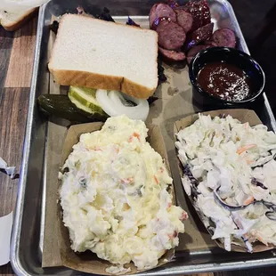 a tray of coleslaw, pickles, and a sandwich