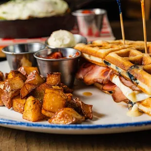 a plate of waffles, bacon, and potatoes