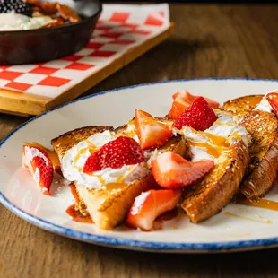 a plate of french toast with strawberries and whipped cream