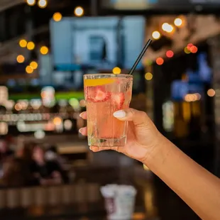 a person holding a glass of water with strawberries and lemon