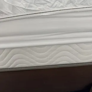 The top-most layer of the fitted sheet with the mattress pad/protector underneath and the mattress itself exposed.