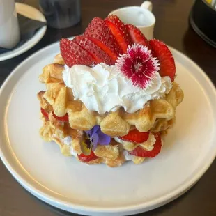 Freshly made waffle, juicy strawberries, whipped cream, and an edible flower.