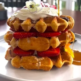 Golden-brown waffles, layered with fresh strawberries, a dollop of whipped cream, and a drizzle of maple syrup.