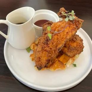 Crispy fried chicken on golden-brown waffles, drizzled with syrup and served with a side of sauce.