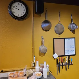 a kitchen counter with a clock and pans hanging on the wall