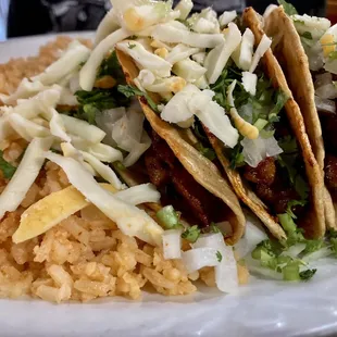 Pork hard shell tacos with cheese, cilantro, and onions. And a side of rice.