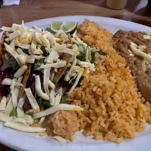 Three hard shell, pork tacos with cheese, cilantro, onions, and a side of rice and beans.