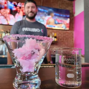 a man behind a bar counter with a glass filled with cotton candy floss