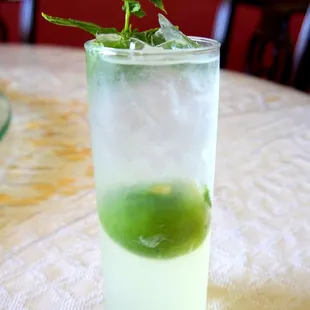 a tall glass with a green drink garnished with a sprig of mint