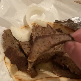a hand holding a piece of meat on a pita