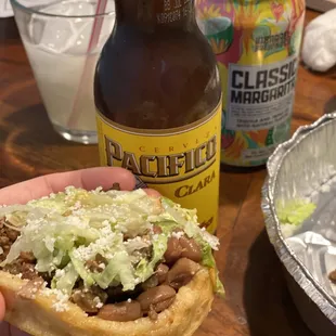 a hand holding a sandwich and a bottle of beer