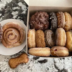 Cinnamon roll, apple fritters, dog treat and a dozen various donuts