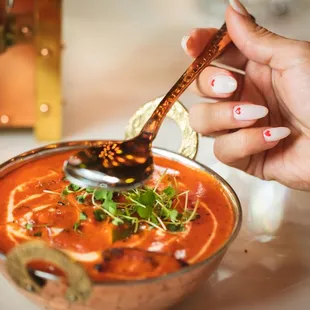 a person holding a spoon over a bowl of soup