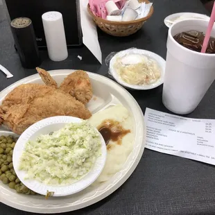 a plate of fried chicken, mashed potatoes, peas, and a drink