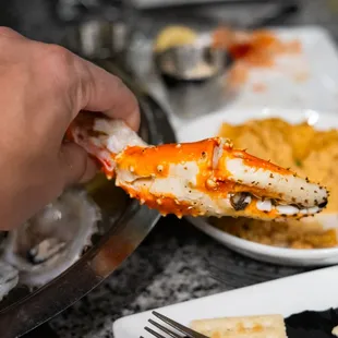 a person holding a piece of crab over a plate of food