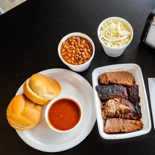 a plate of ribs, beans, coleslaw, and a sandwich