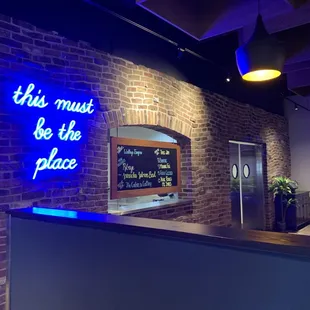 a brick wall with a neon sign that says this must be the place