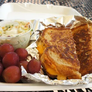 a grilled cheese sandwich with grapes and coleslaw