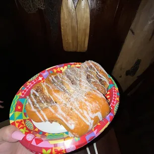 a person holding a paper plate with a pastry on it