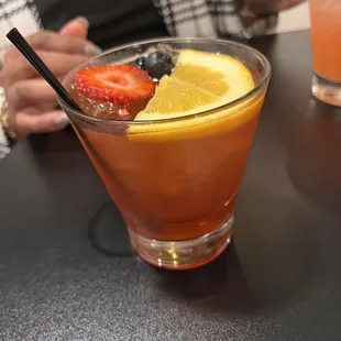 a glass of orange juice with strawberries and lemon wedges