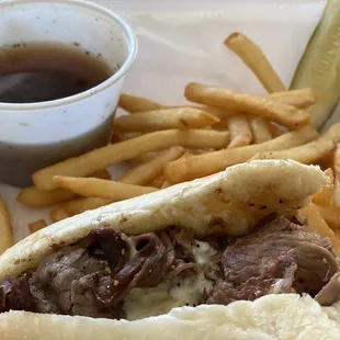 Half of the roast beef sandwich with cheese,  fries and dipping juice.