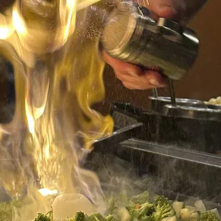 a chef sprinkling sauce over a dish of broccoli