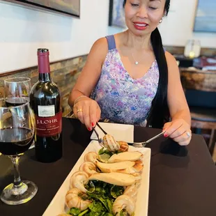 a woman sitting at a table with a plate of food and a glass of wine