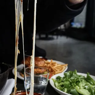 a person holding a piece of cheese over a bowl of soup